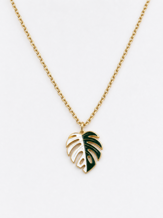 A gold chain necklace featuring a monstera leaf pendant with dark green enamel accents, shown against a plain white background. plant jewelry